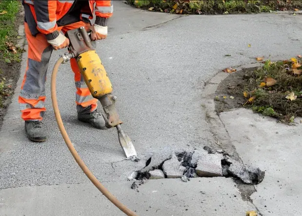 Worker breaking out damaged concrete with a demolition hammer